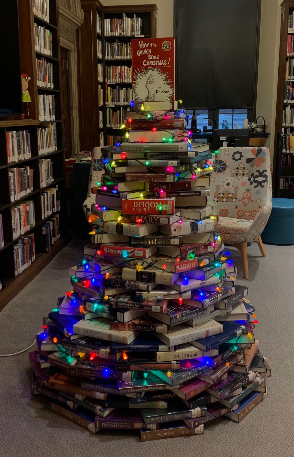 Book tree with Christmas lights strung around it inside of a library